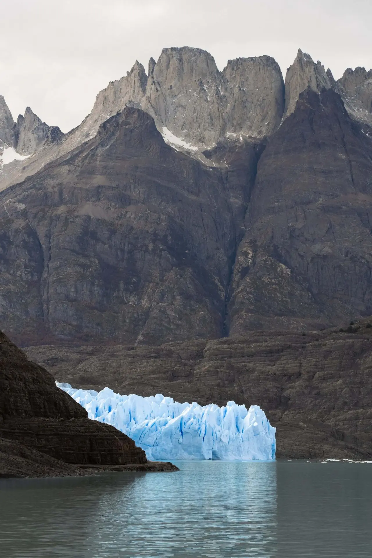 Dramatic mountain landscape with towering rocky peaks and a blue glacier meeting a calm lake