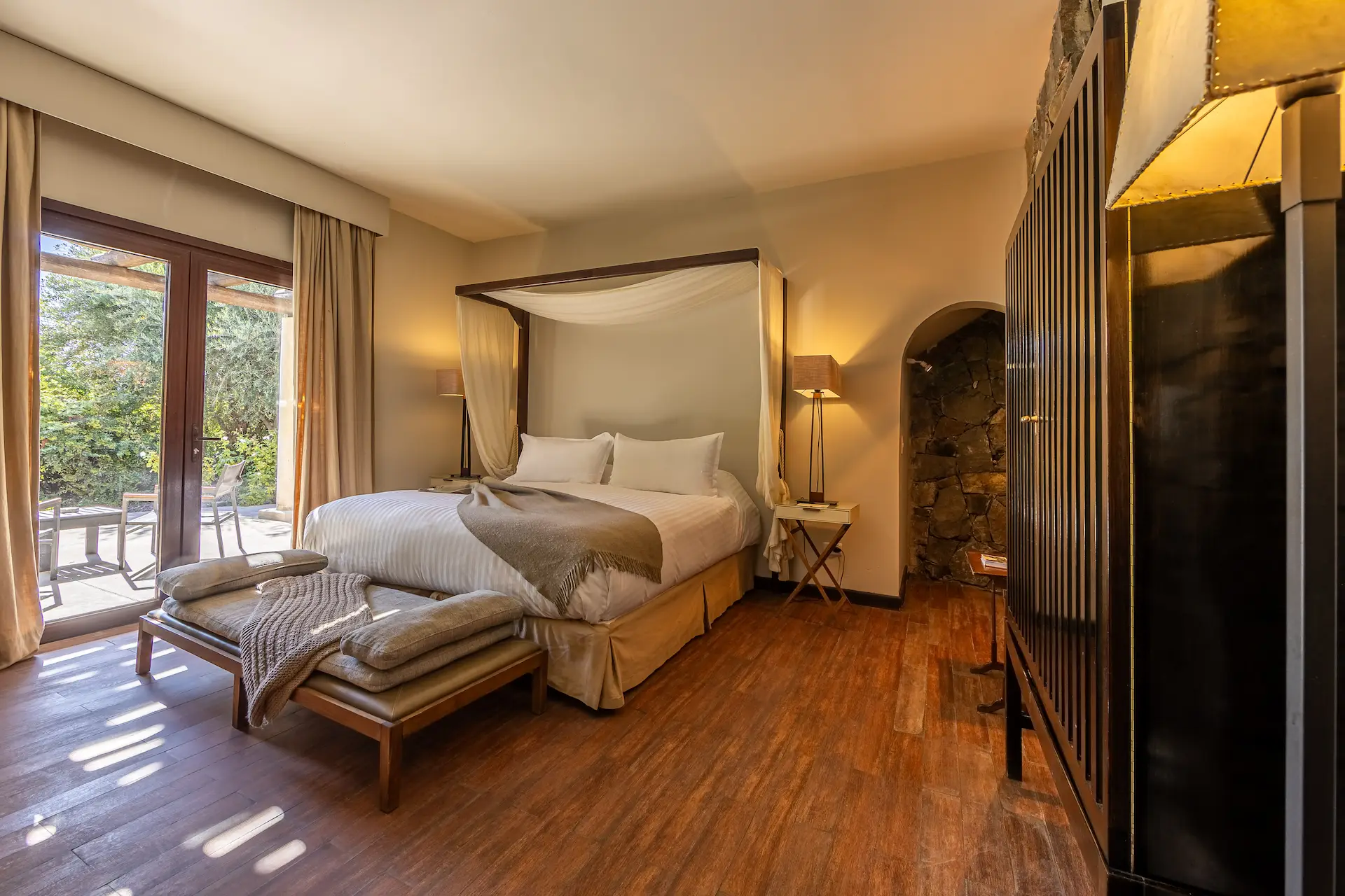 Elegant bedroom with canopy bed wooden floors and natural light from terrace creating a warm relaxing atmosphere