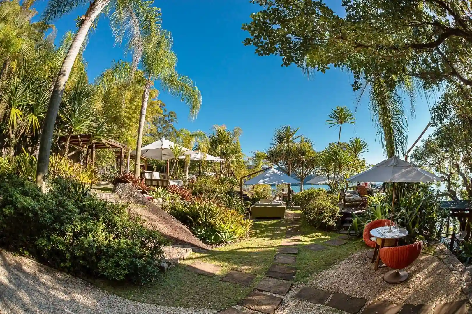 Lush tropical garden with seating areas umbrellas and ocean view under clear blue sky
