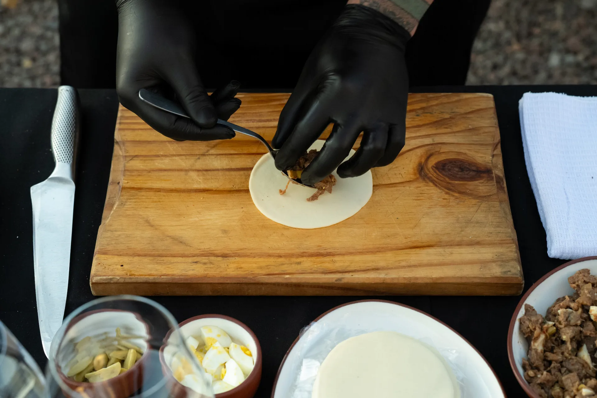 Chef preparing a small dumpling with meat filling on a wooden board with ingredients arranged nearby
