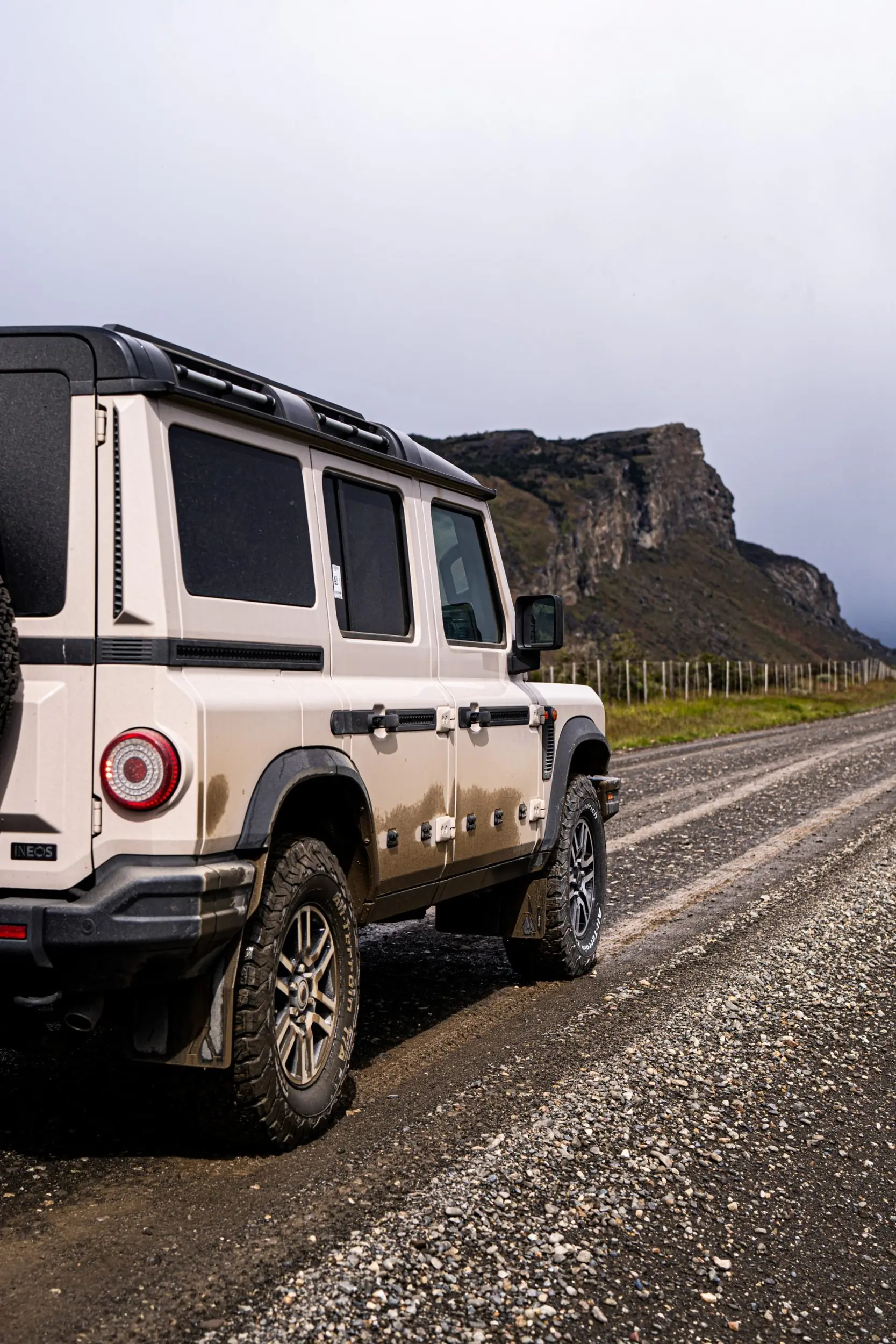 Off-road suv parked on a gravel road beside rugged cliffs under an overcast sky.