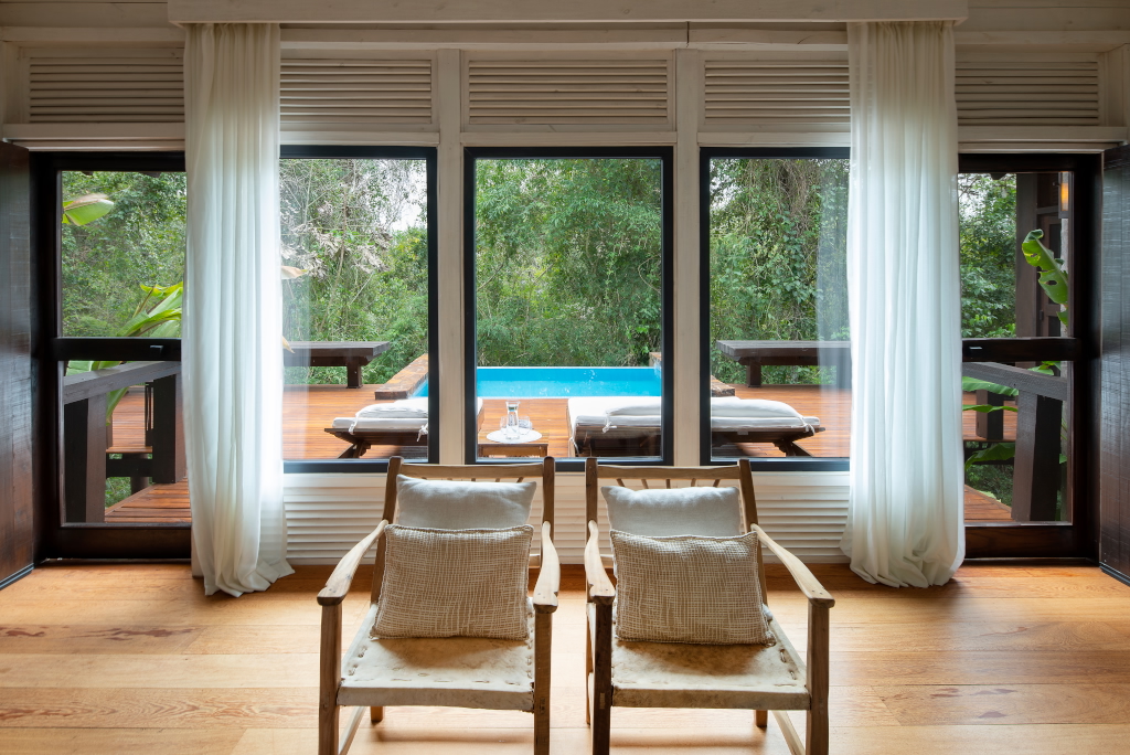 Luxury room with two armchairs facing large windows overlooking a private deck with pool and lush forest view