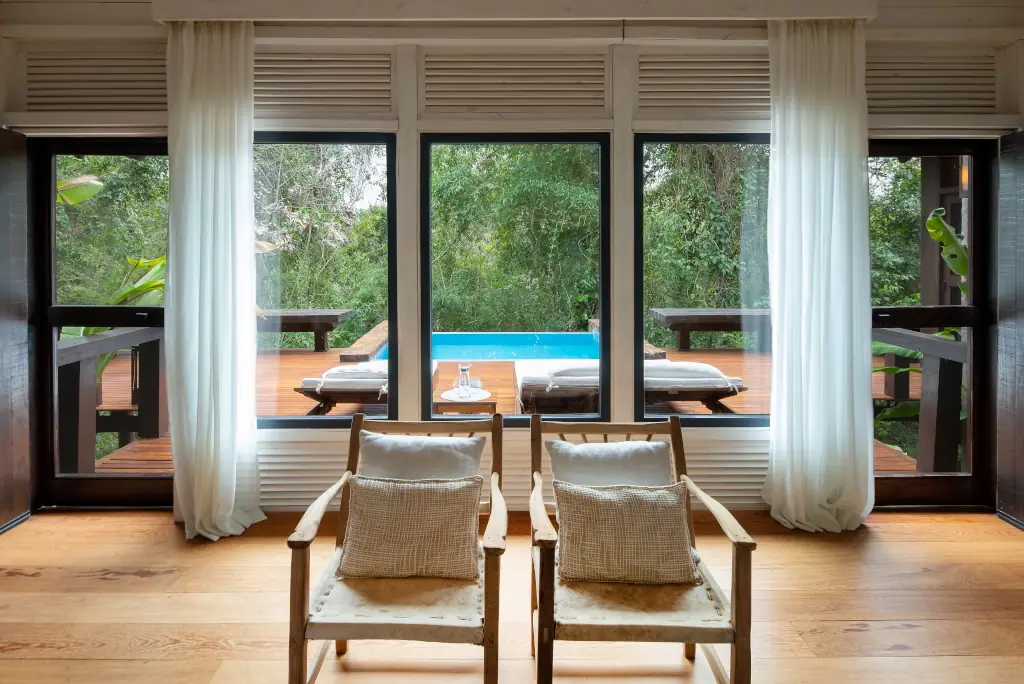 Luxury Room With Two Armchairs Facing Large Windows Overlooking A Private Deck With Pool And Lush Forest View