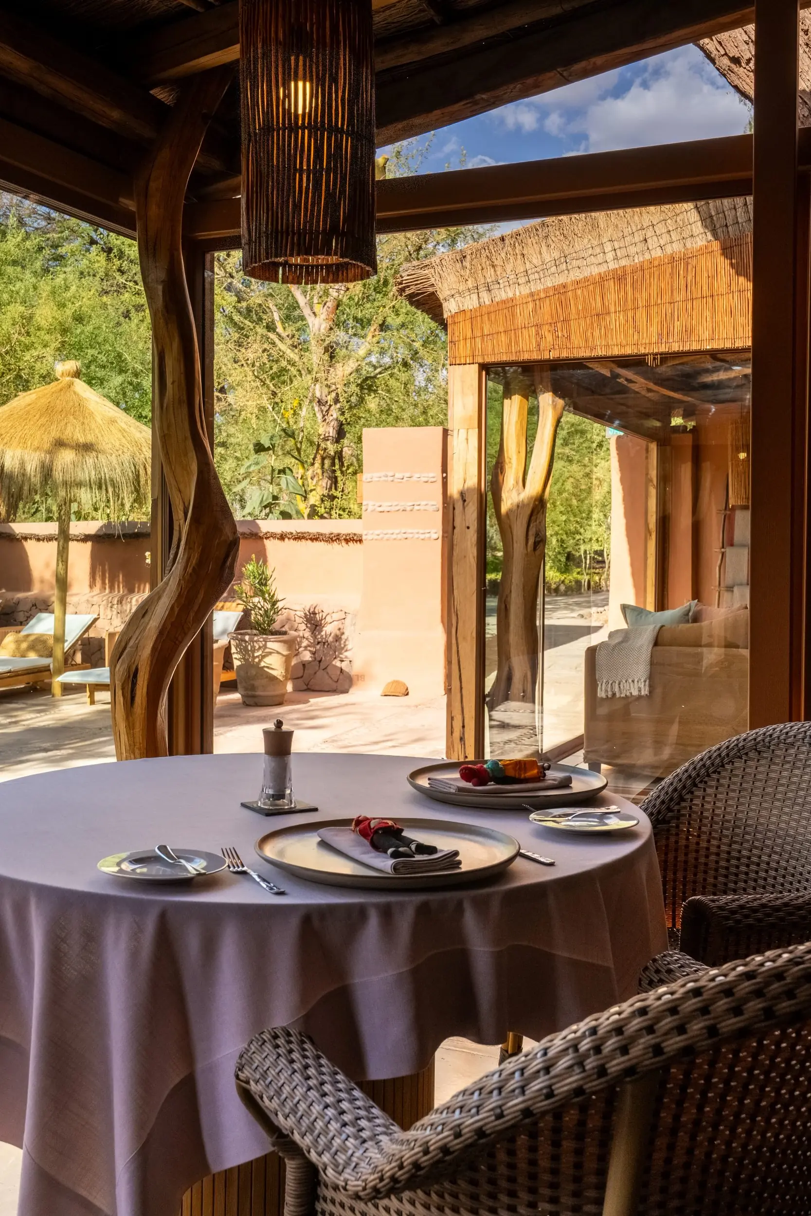 Rustic Open-Air Dining Space With Woven Chairs, Warm Wood Accents, And Views Of A Serene Desert Courtyard.