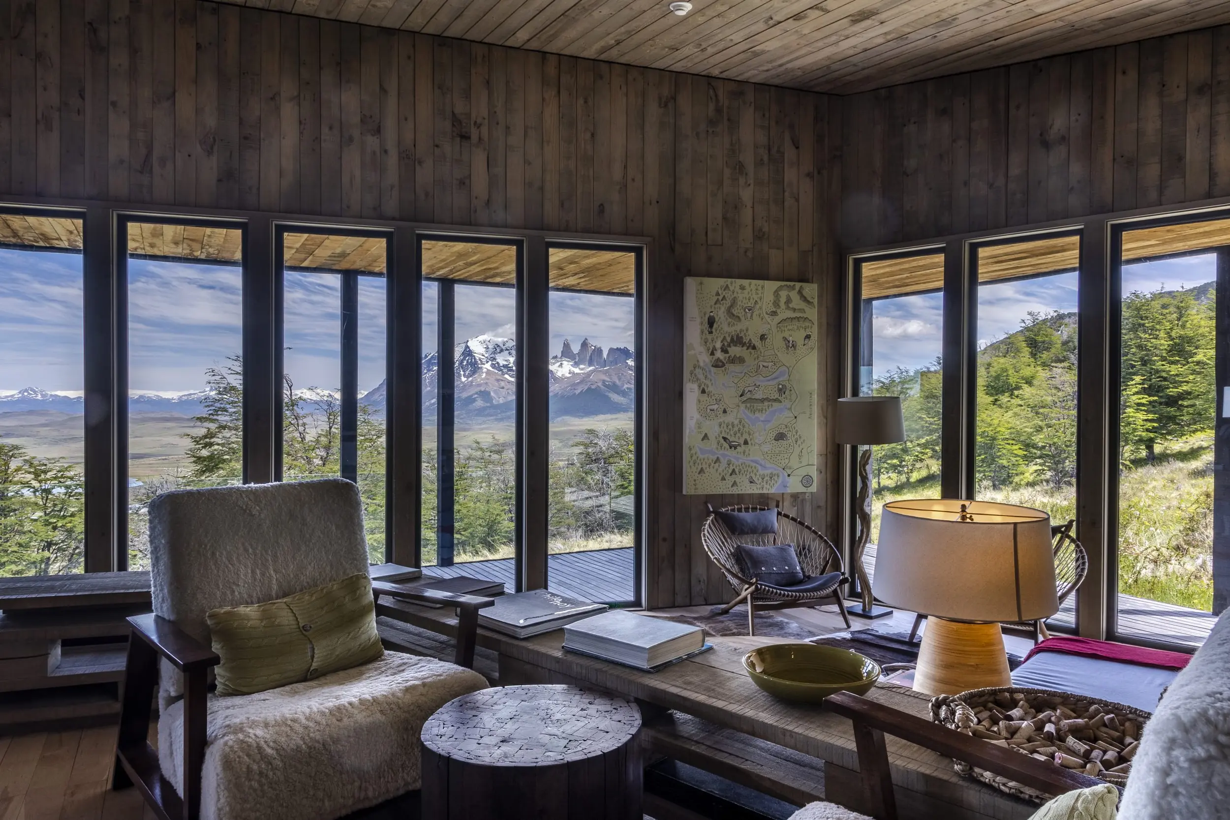 Cozy Wood-Paneled Cabin Living Room With Panoramic Mountain Views Through Floor-To-Ceiling Windows.