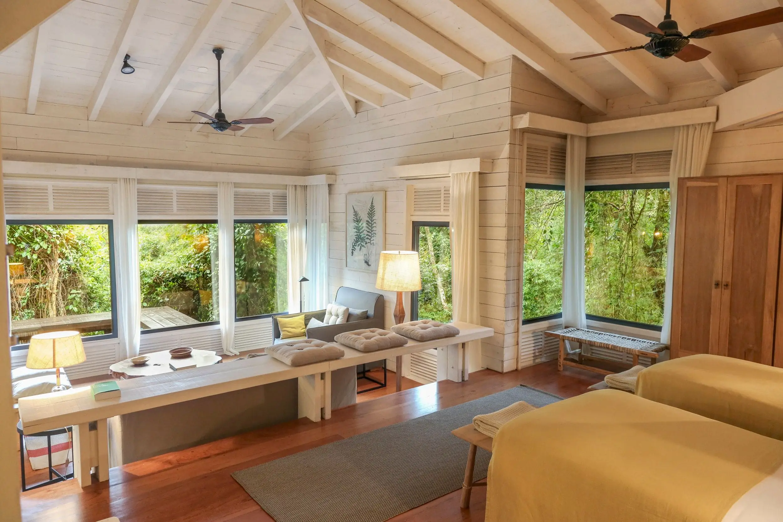 Bright Spa Treatment Room With Massage Tables, Vaulted Ceilings, And Large Windows Overlooking Lush Greenery.