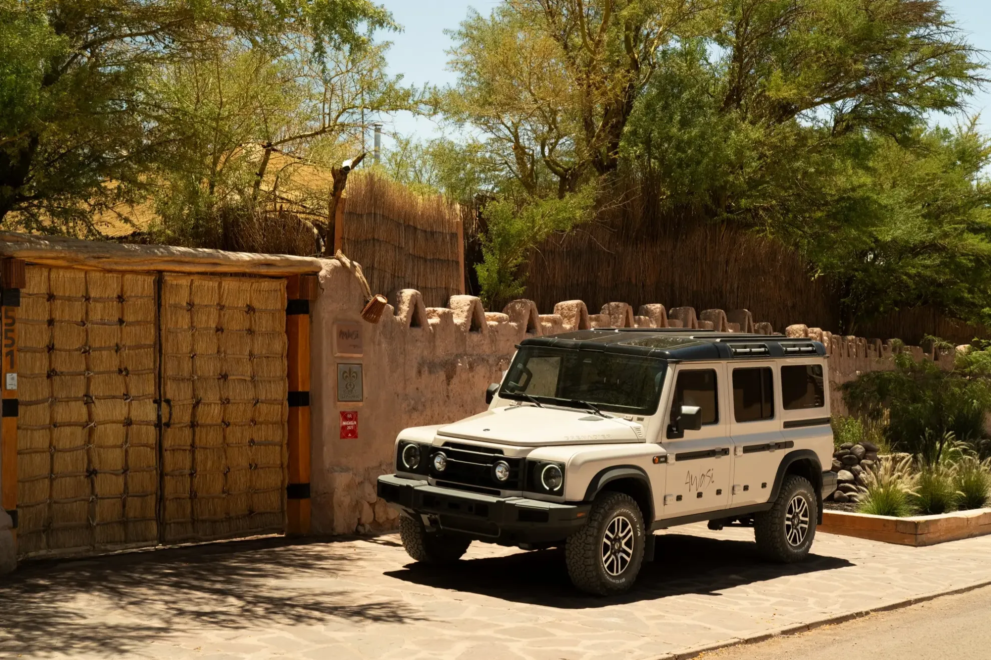 White off-road suv parked outside a rustic desert lodge surrounded by trees and adobe-style walls.