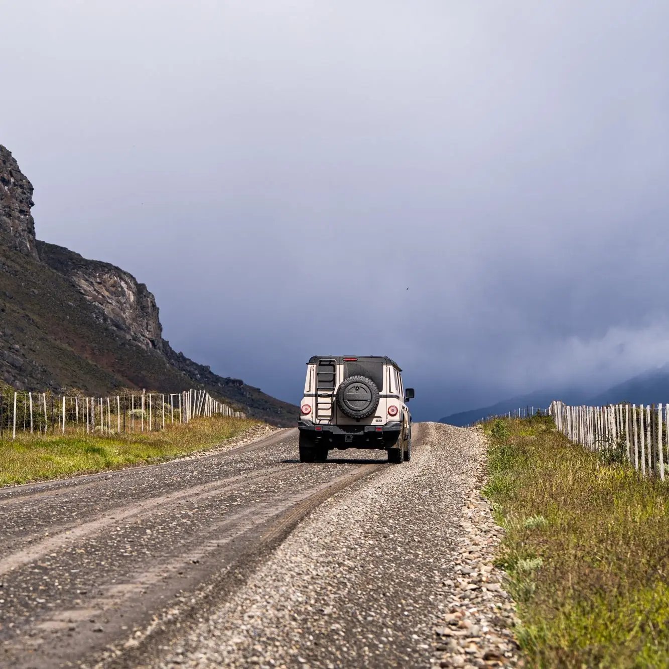 Off-road suv driving along a gravel road through a mountainous landscape under cloudy skies.