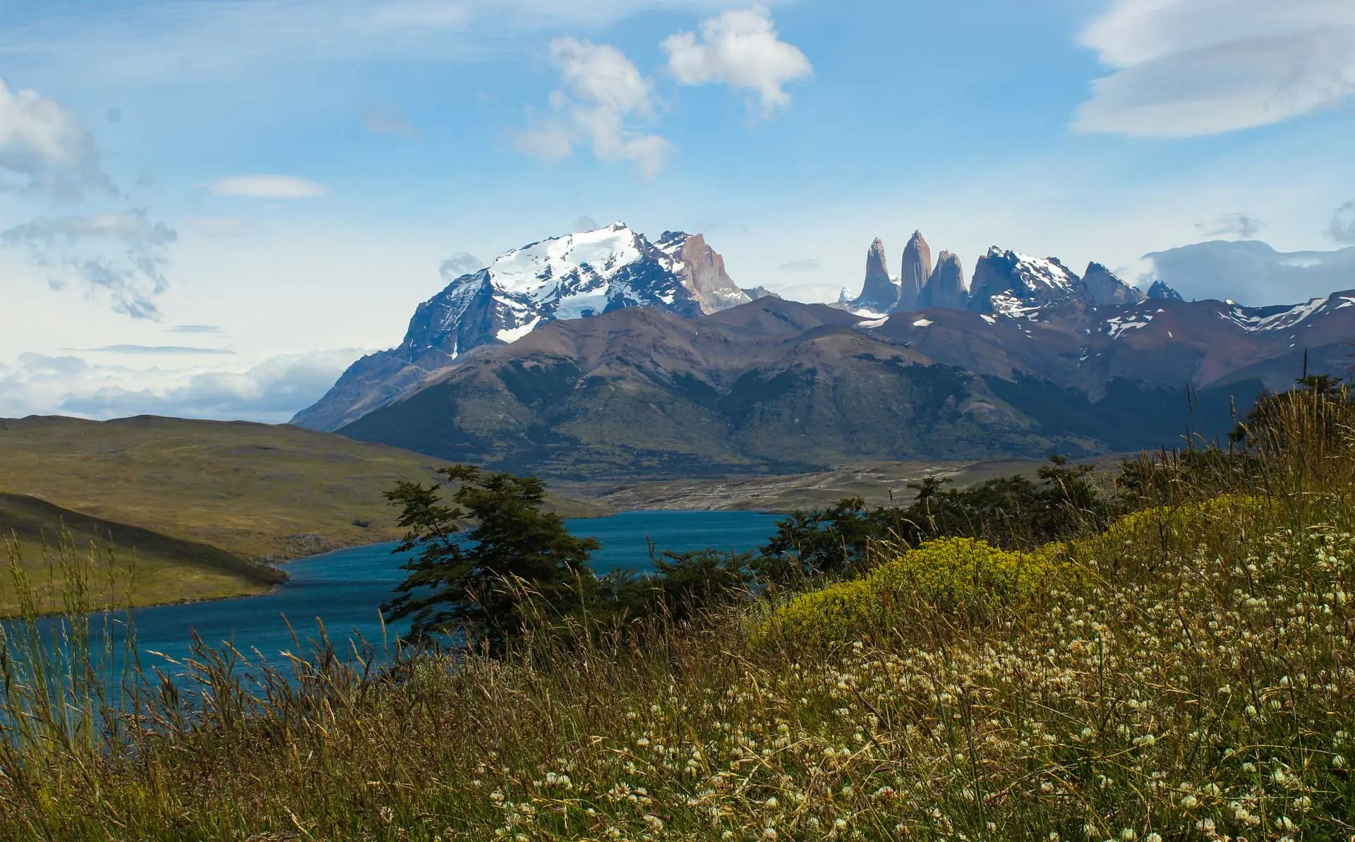 A Bright Blue Lake Lies Before Rugged, Snow-Capped Mountain Peaks Under A Cloudy Sky.