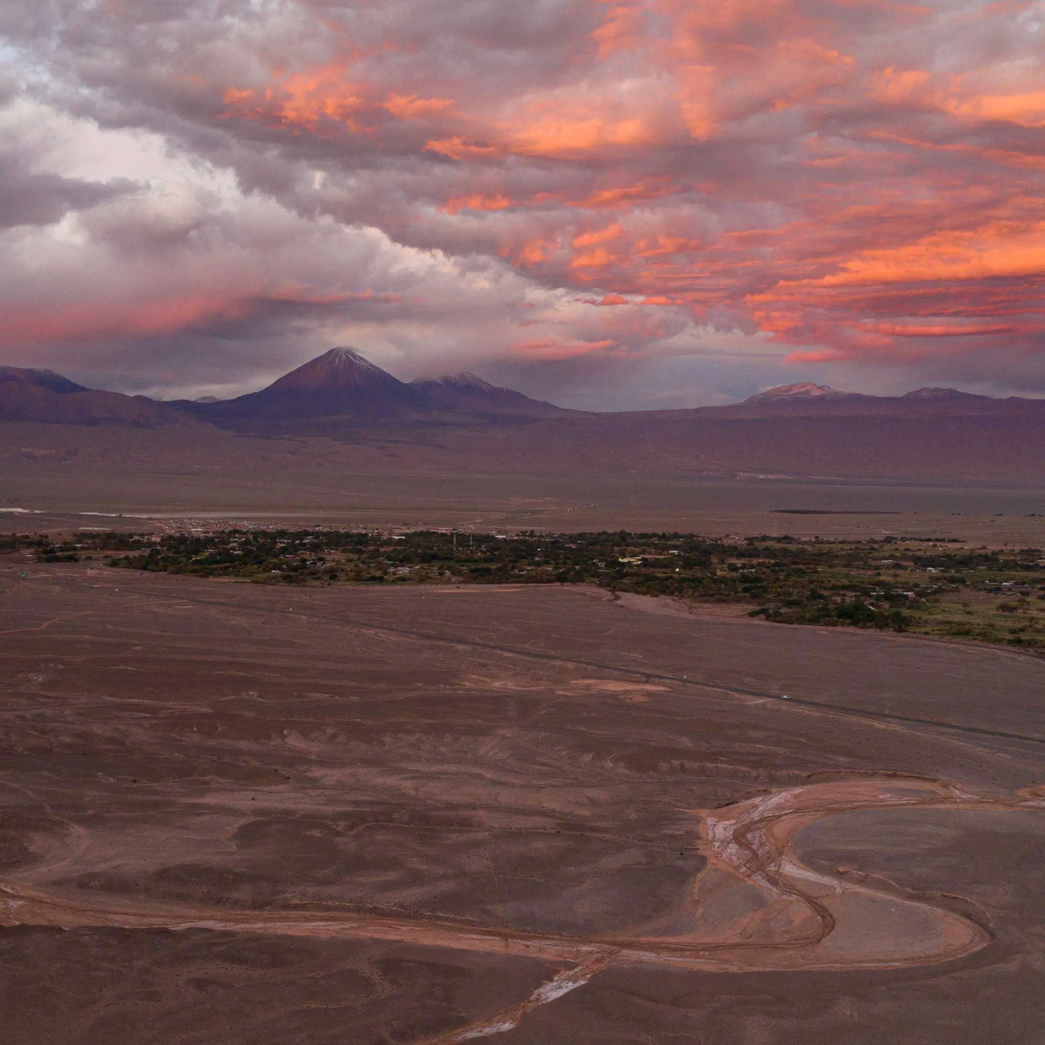An Aerial View Of A Desert Valley Beneath A Vibrant Pink Sunset Sky.