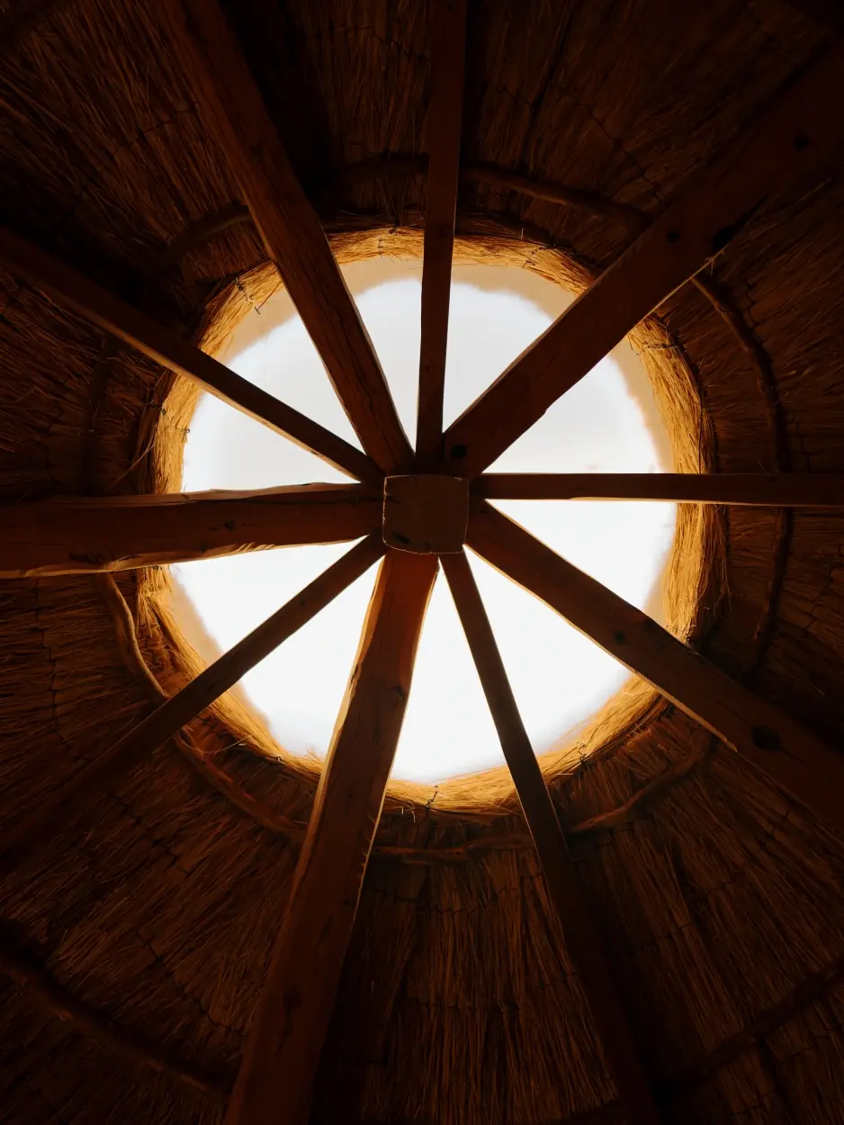Wooden Beams Radiate Outward From The Center Of A Circular Skylight In A Thatched Roof.