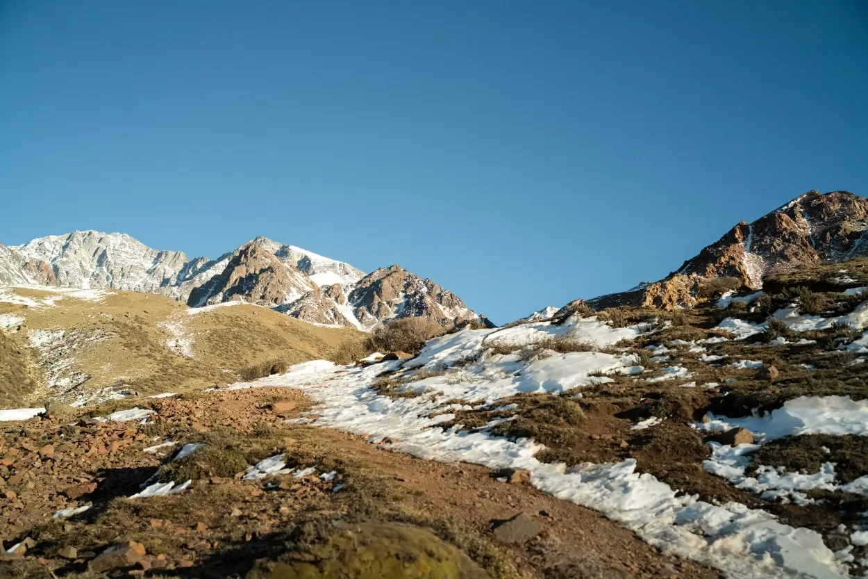 Snow-Dusted Mountain Peaks And Rocky Terrain Under A Clear Blue Sky.