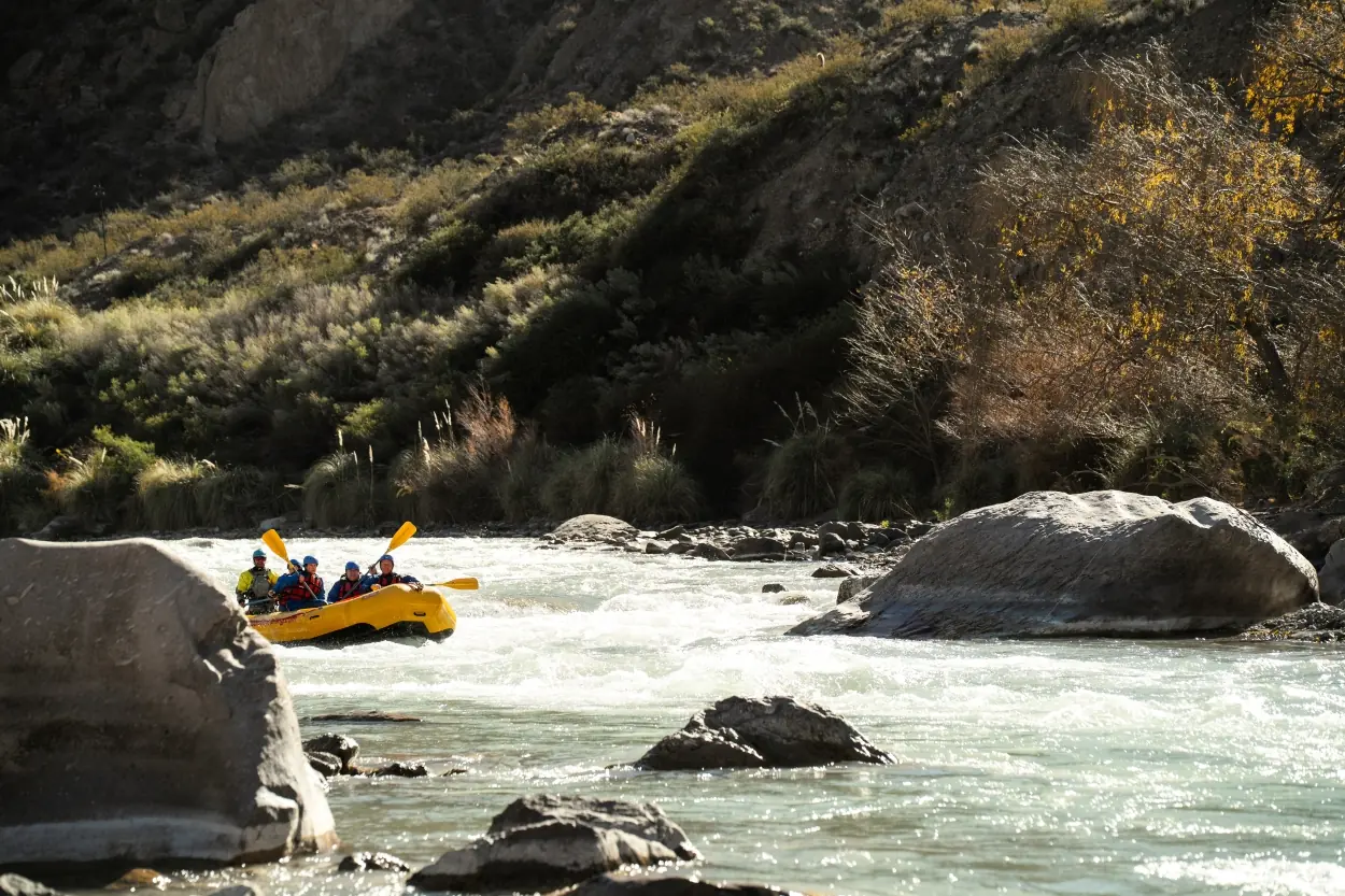 Group Rafting Through Whitewater Rapids On A Rocky River Surrounded By Rugged Hills And Trees.