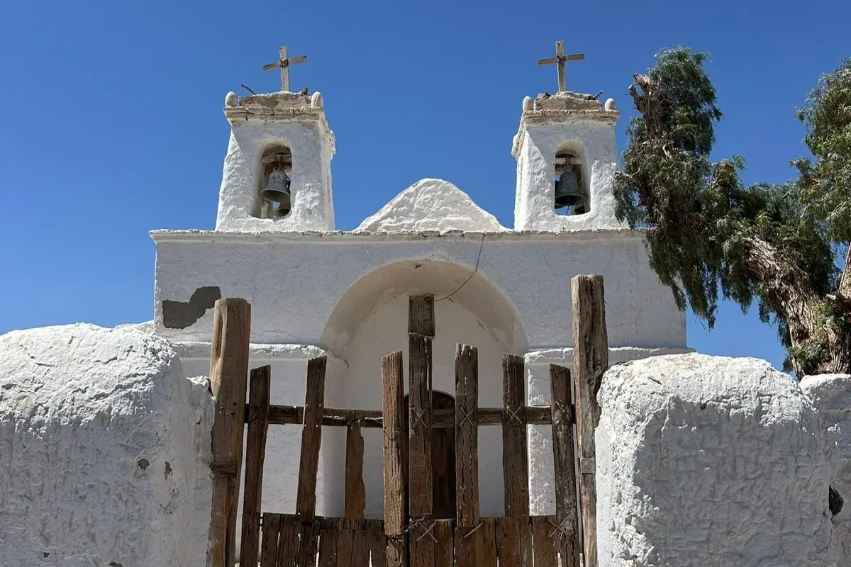 A Rustic Wooden Gate Stands Before A Historic White Church With Twin Bell Towers.