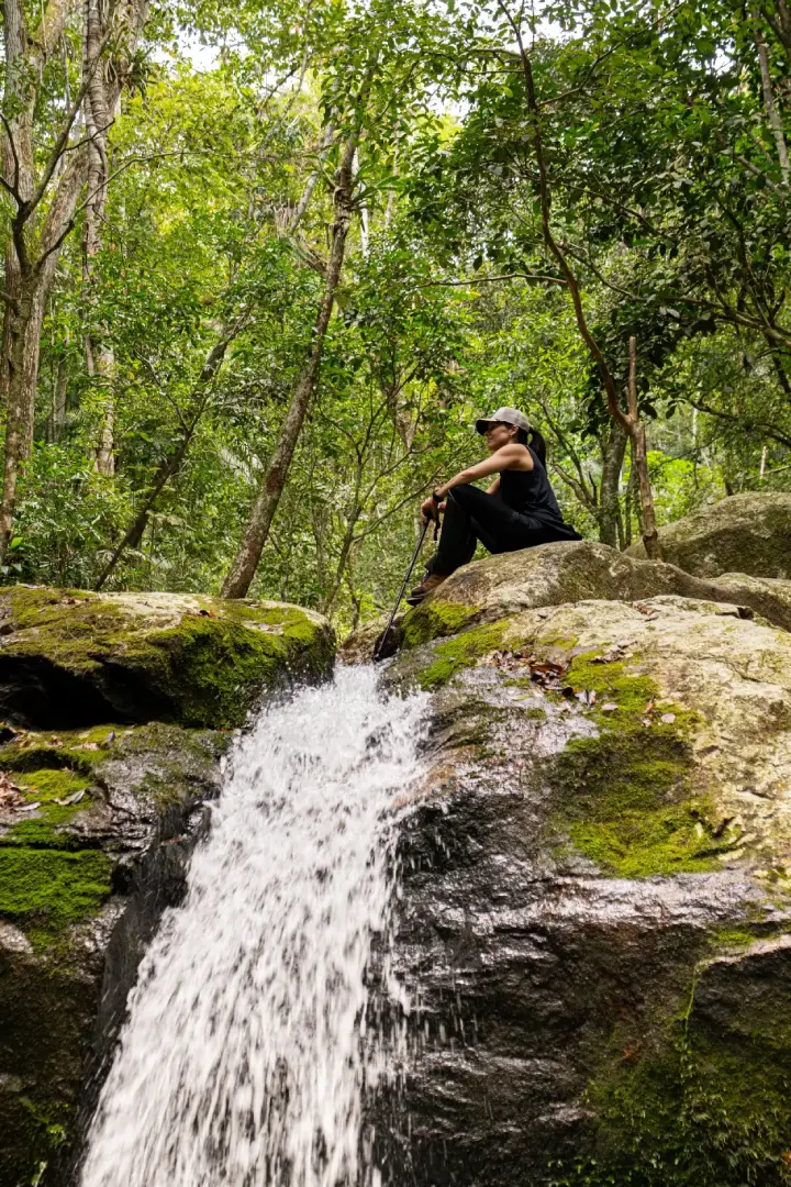 A Hiker Sits On A Mossy Boulder Beside A Rushing Forest Waterfall.