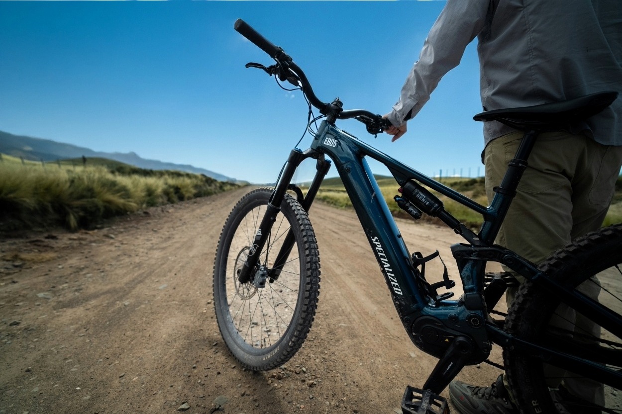 Person Standing With An Electric Mountain Bike On A Dirt Road In An Open Rural Landscape.