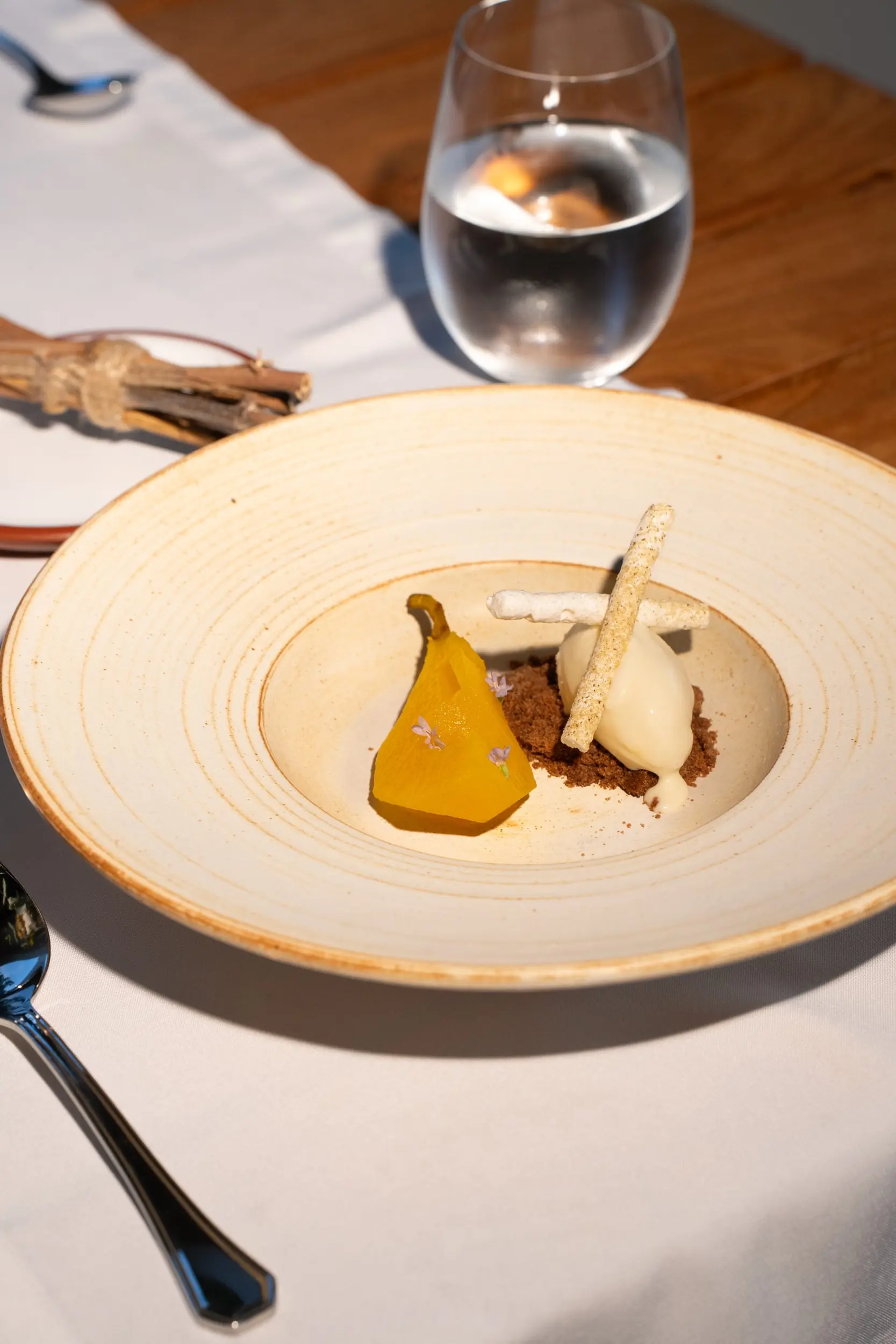 A Gourmet Dessert Features A Poached Pear Slice And Vanilla Ice Cream Over Chocolate Crumbles In A Wide Beige Bowl.