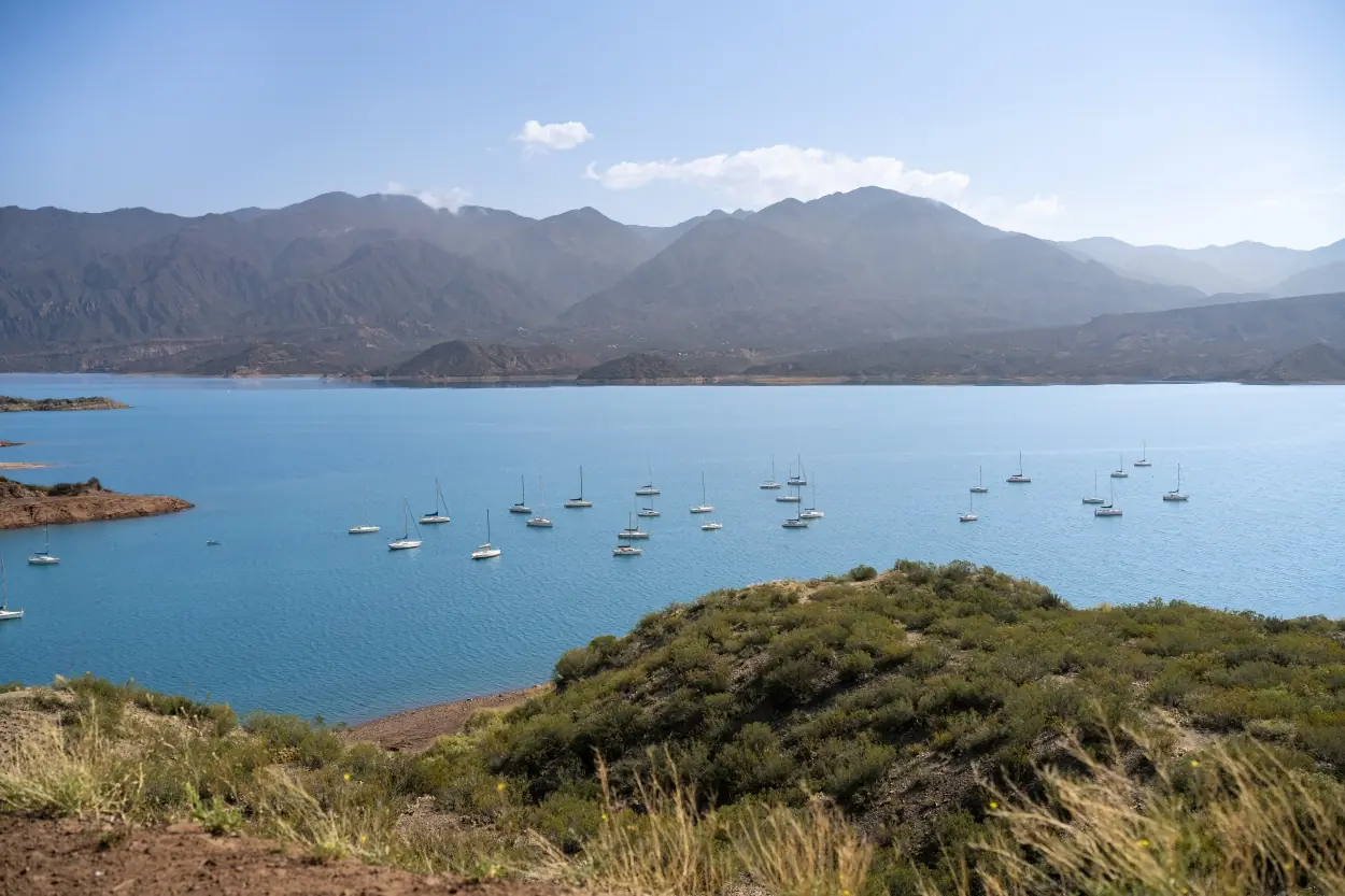 Wide View Of Sailboats On A Blue Lake Surrounded By Mountains And Dry Green Hills.