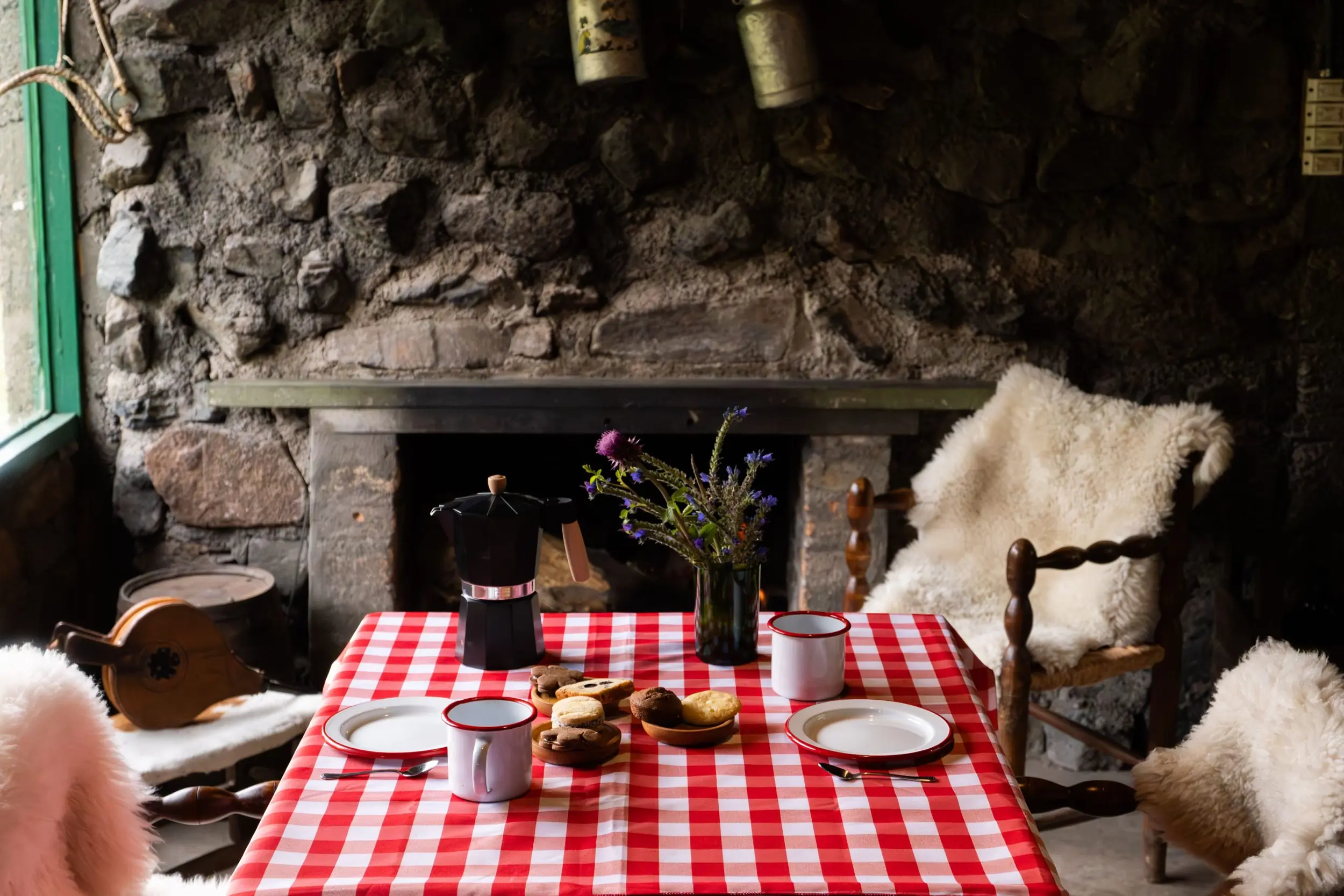 A Rustic Breakfast Table With A Red-And-White Checkered Tablecloth Features Coffee And Pastries Before A Stone Fireplace.