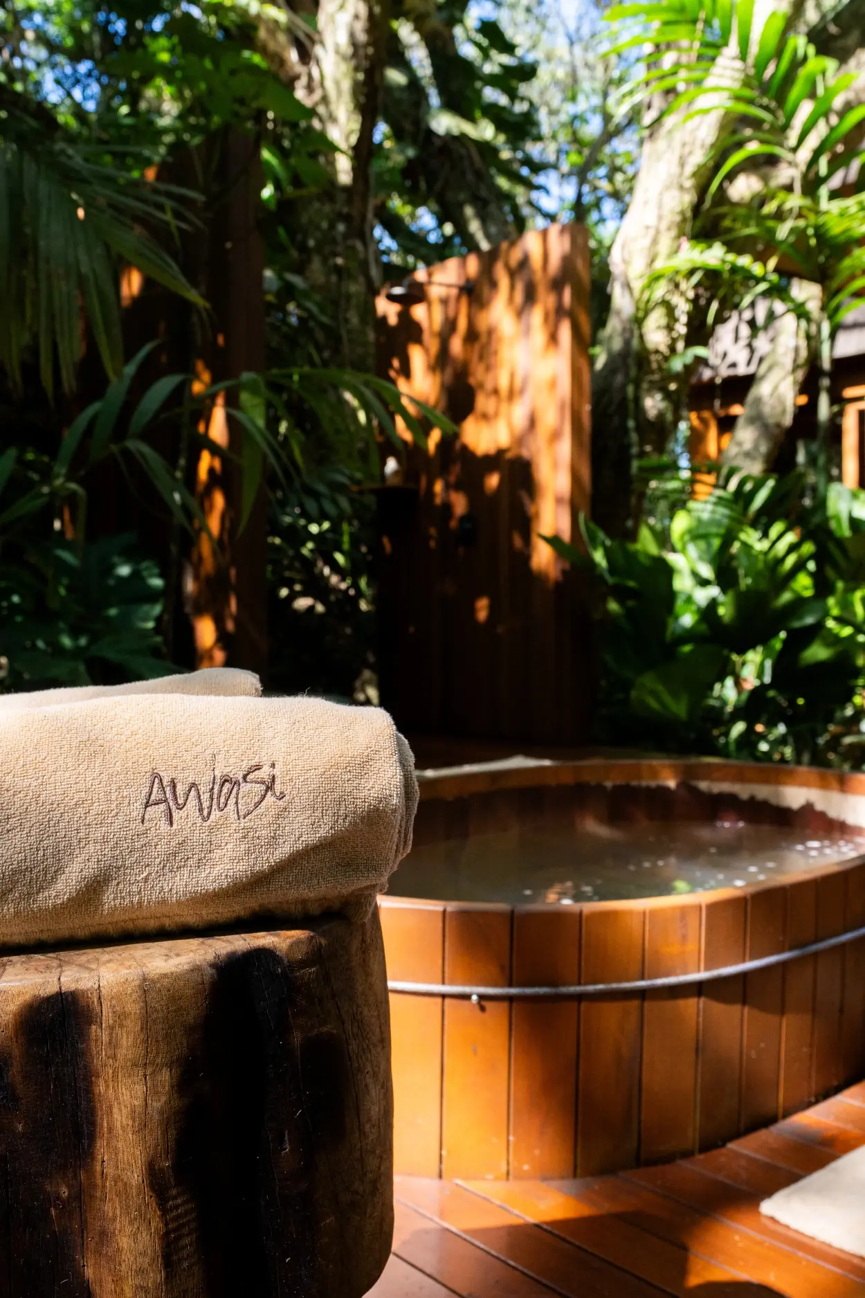 An Embroidered Towel Sits On A Wooden Stump Beside An Outdoor Hot Tub Surrounded By Lush Green Foliage.