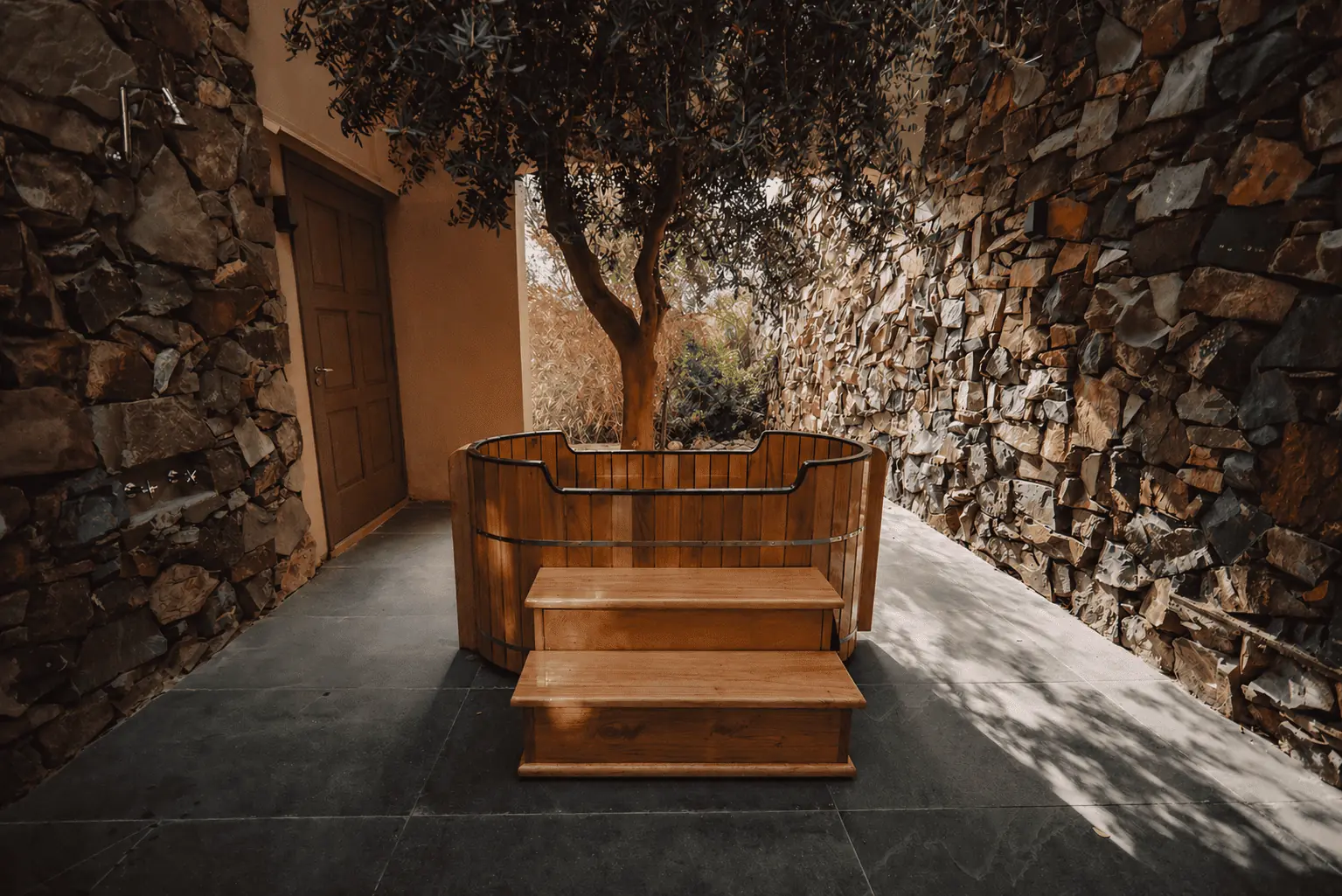 An Outdoor Wooden Hot Tub With Steps Between Two Rustic Stone Walls.